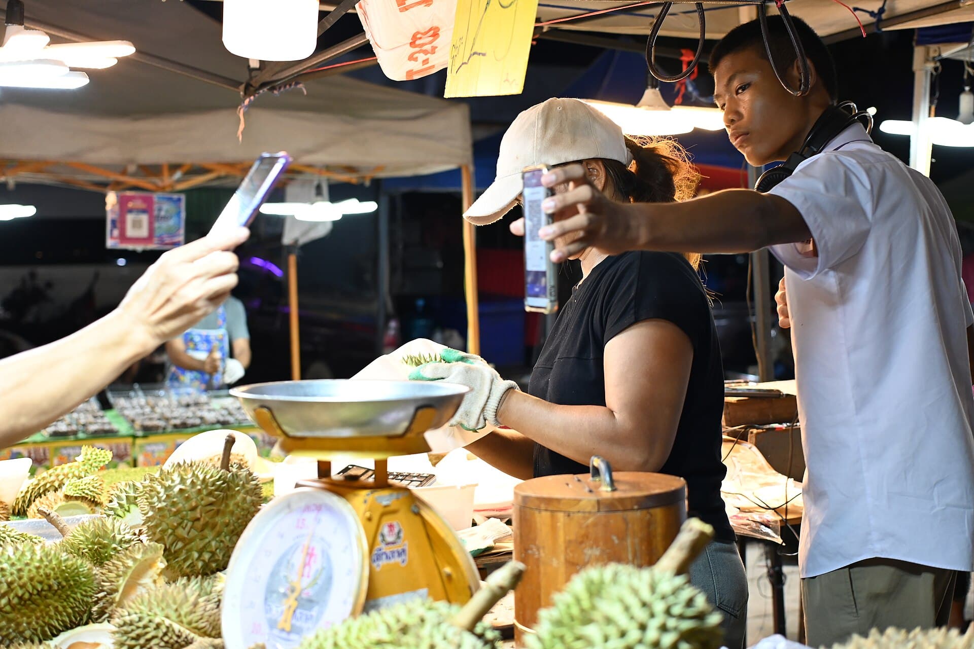 A buyer holding up a phone to scan at a night market stall in Thailand